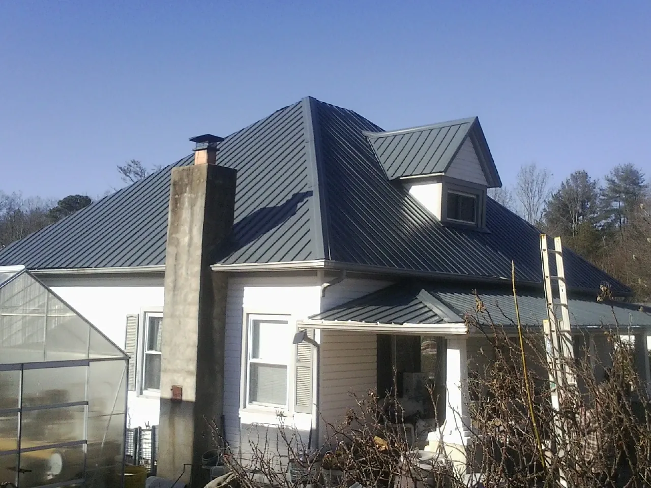 Dark blue standing seam metal roof on a white farmhouse with dormer — Slate & Tile Roof Repair by Roofing Brothers in Dutton