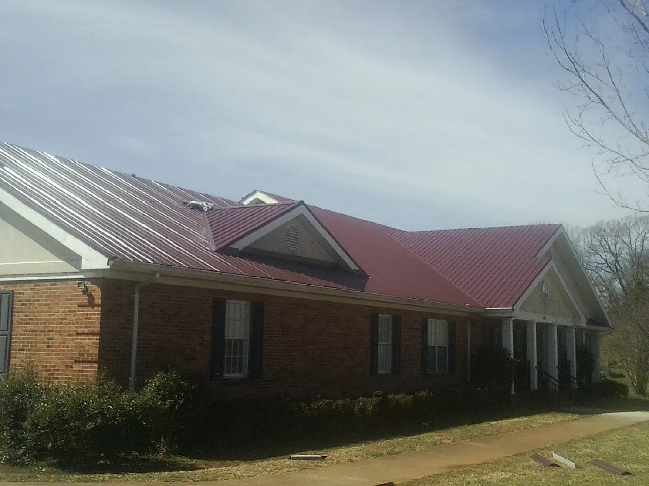 Red metal roof with gabled entries on a long brick building, from a Hail Damage Roof Repair job in Dutton