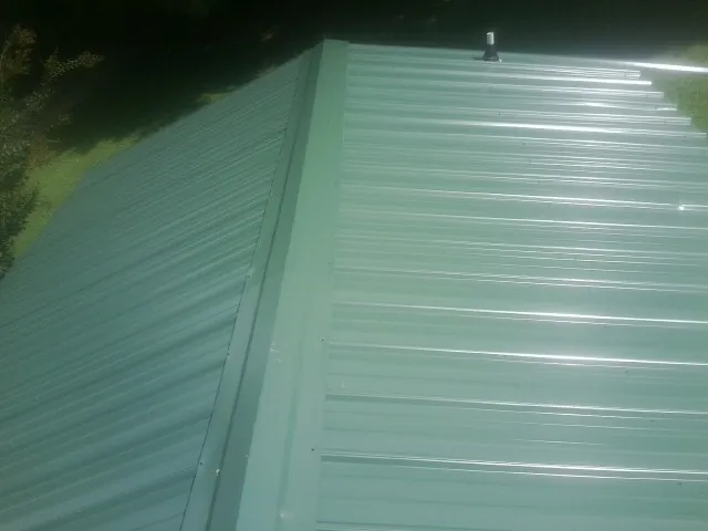 New green metal panels meeting at the ridge of a roof — Flat Roof Repair work by our crew in Dutton