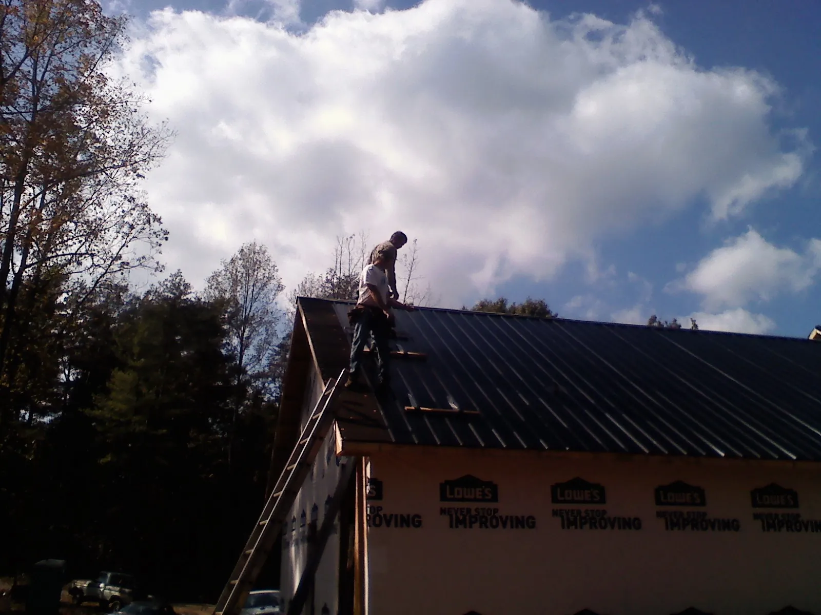 Roofer fastening dark metal panels high against a cloudy sky, from a Roof Inspection job in Dutton
